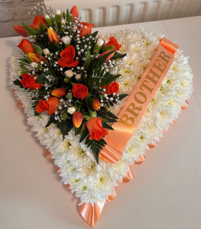 Massed Heart - A touching heart-shaped funeral tribute created to honour the memory of a loved one. Featuring a classic white base accented with warm peach and orange tones, this elegant arrangement symbolises love, admiration, and the special bond that will never be forgotten.

Finished with a personalised ribbon this heartfelt design offers a meaningful expression of sympathy and remembrance. Handcrafted with care, it serves as a beautiful focal tribute at funeral services, memorial ceremonies, and celebrations of life.